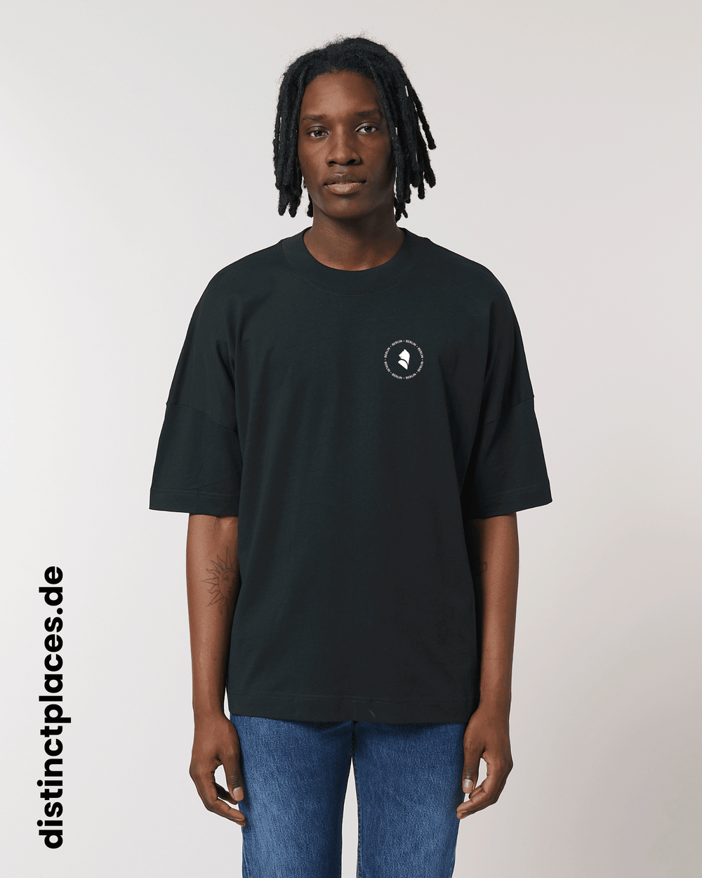 Mann von vorne trägt schwarzes fairtrade, vegan und bio-baumwoll T-Shirt mit einem minimalistischem weißen Logo, beziehungsweise Wappen und Schriftzug für Berlin