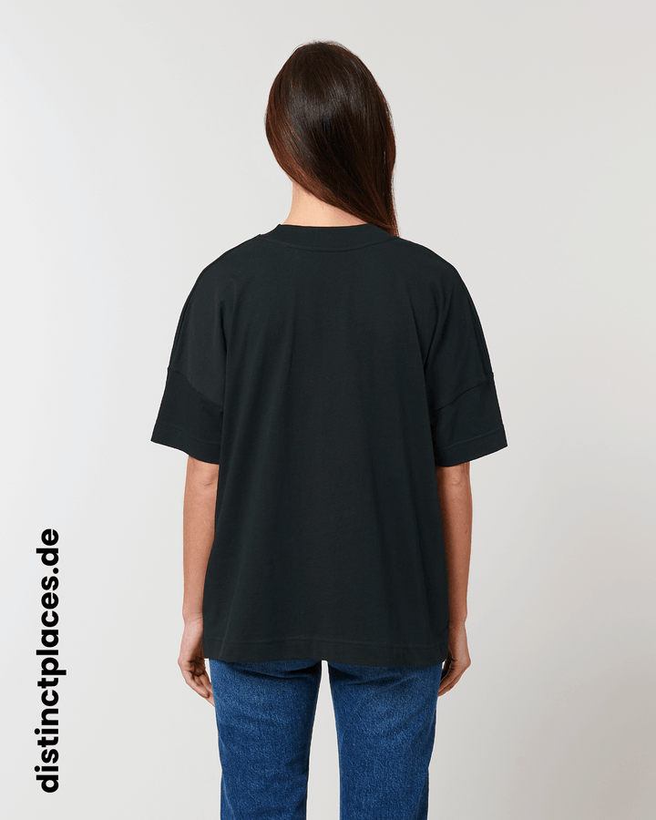 Frau von hinten trägt schwarzes fairtrade, vegan und bio-baumwoll Oversized T-Shirt mit einem minimalistischem weißen Logo, beziehungsweise Schriftzug für Bremen