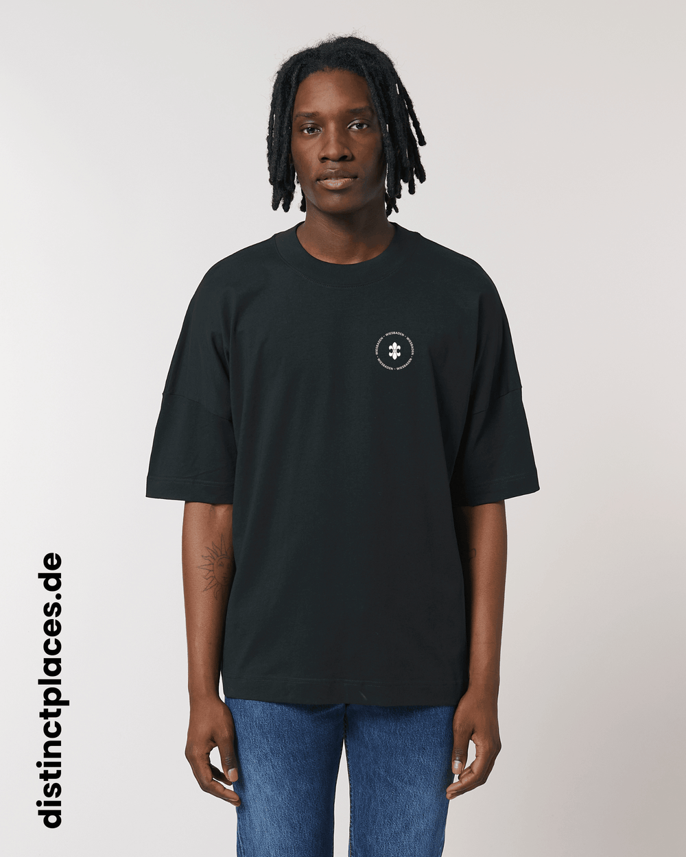 Mann von vorne trägt schwarzes fairtrade, vegan und bio-baumwoll T-Shirt mit einem minimalistischem weißen Logo, beziehungsweise Wappen und Schriftzug für Wiesbaden